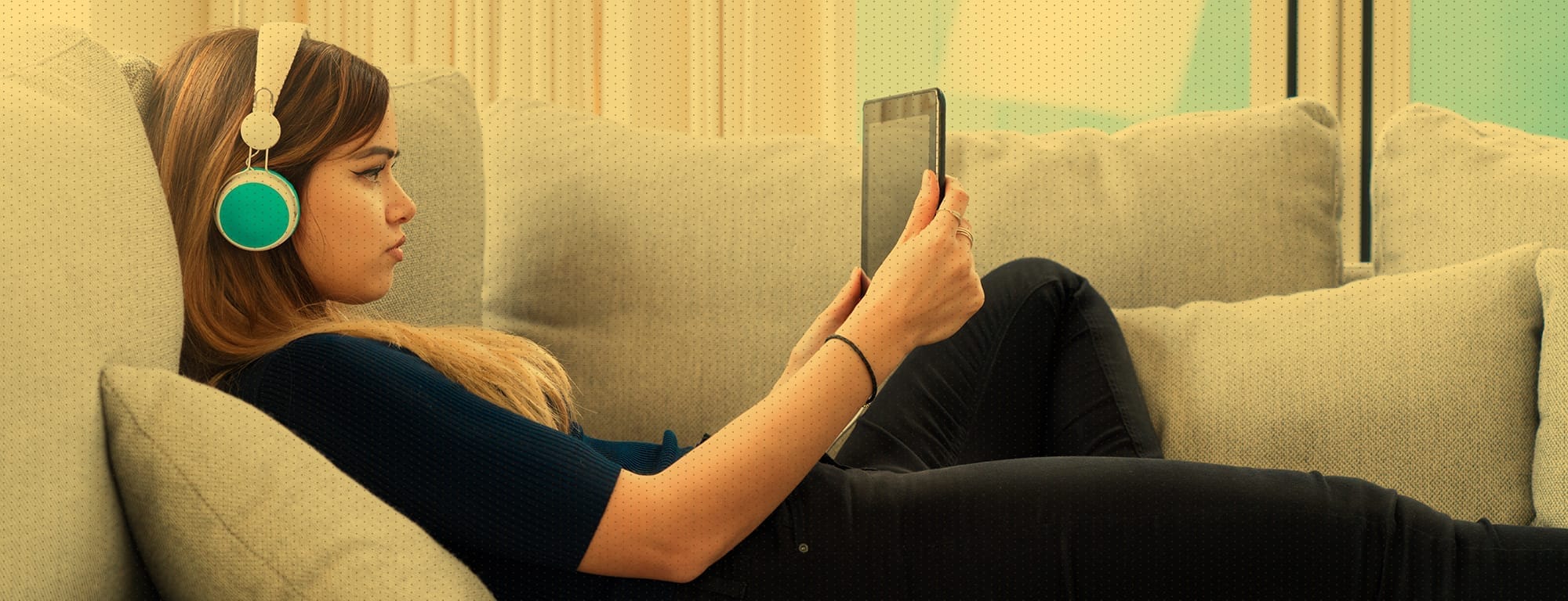 A young woman wearing headphones looking at a tablet she holds in her hand