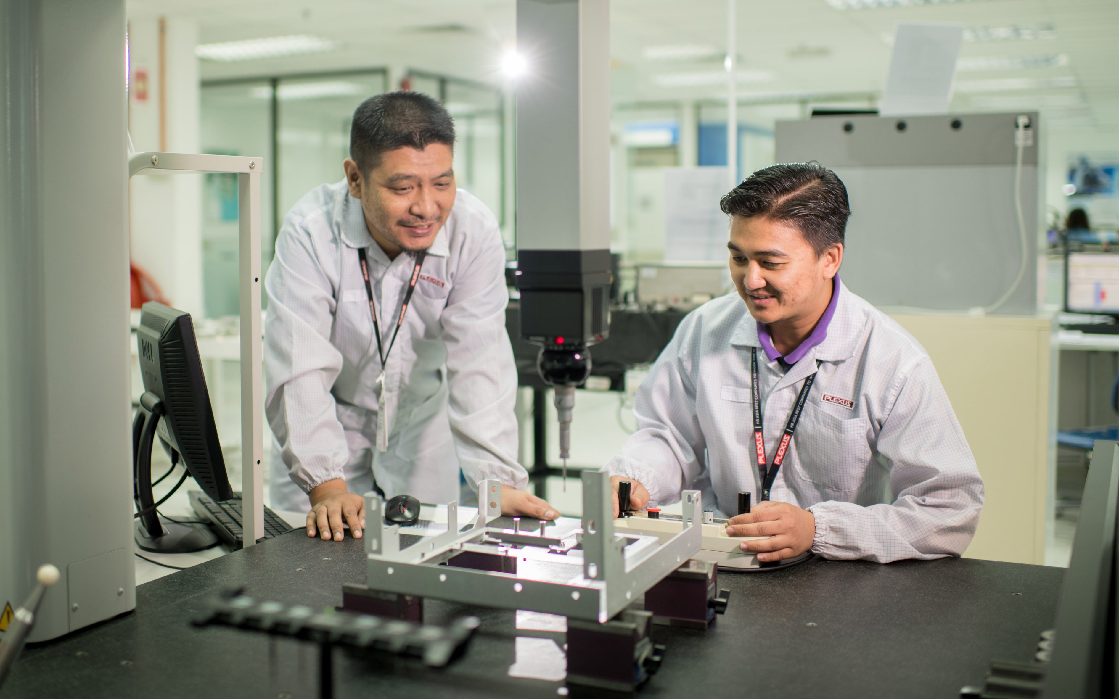 Two Plexus engineers working in a Failure Analysis Lab to inspect a complex assembly for precision and quality control.