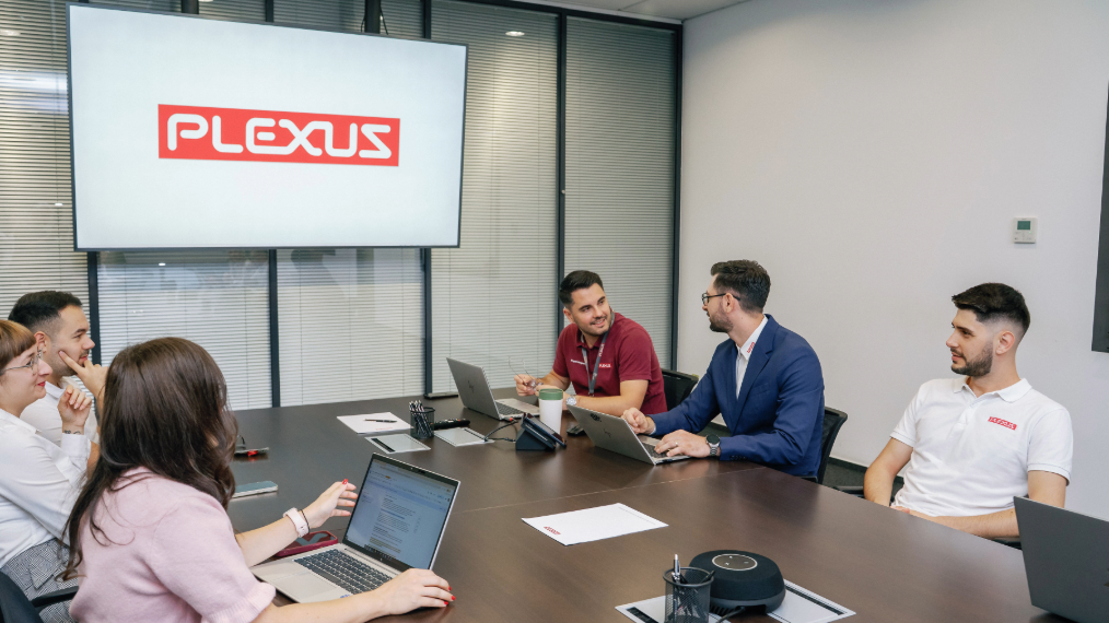A diverse group of six professionals seated around a conference room table with open laptops, engaged in a collaborative team meeting.